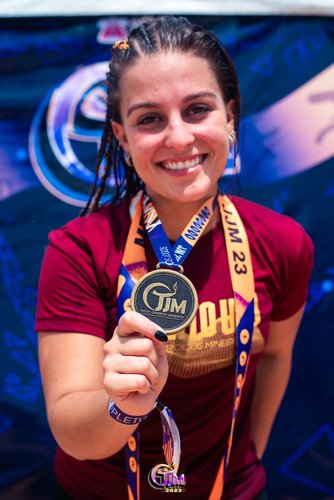 Atleta Ana Júlia Campos, sorrindo e mostrando a medalha que conquistou