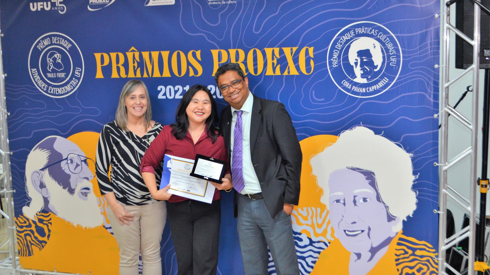 Professora Elaine Kikuti (ao centro), exibindo certificado ao lado da diretora de Extensão e do pró-reitor de Extensão e Cultura