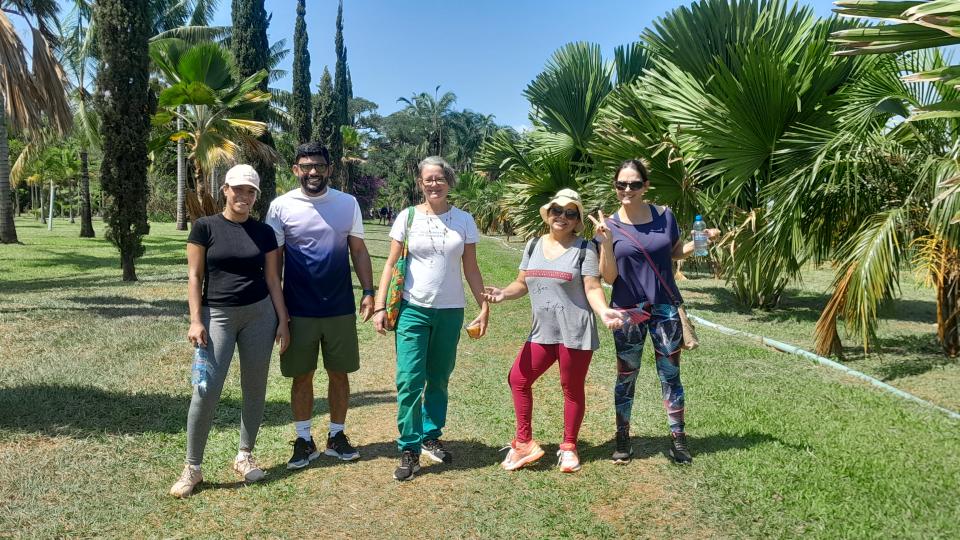 Imagem mostra os participantes da Caminhada Ecológica em meio a natureza, conhecendo o Campus Glória e registrando fotos da atividade. 