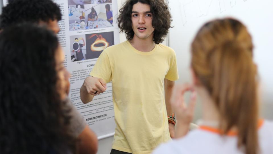 A imagem mostra estudante fazendo explicação de pesquisa 