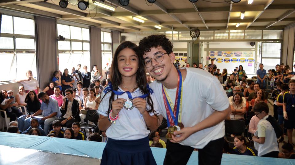 Dois alunos (um menino e uma menina) posam para a foto com suas medalhas