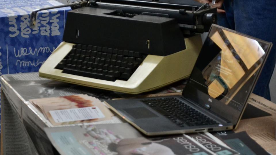 Máquina de escrever e computador em cima de uma mesa.
