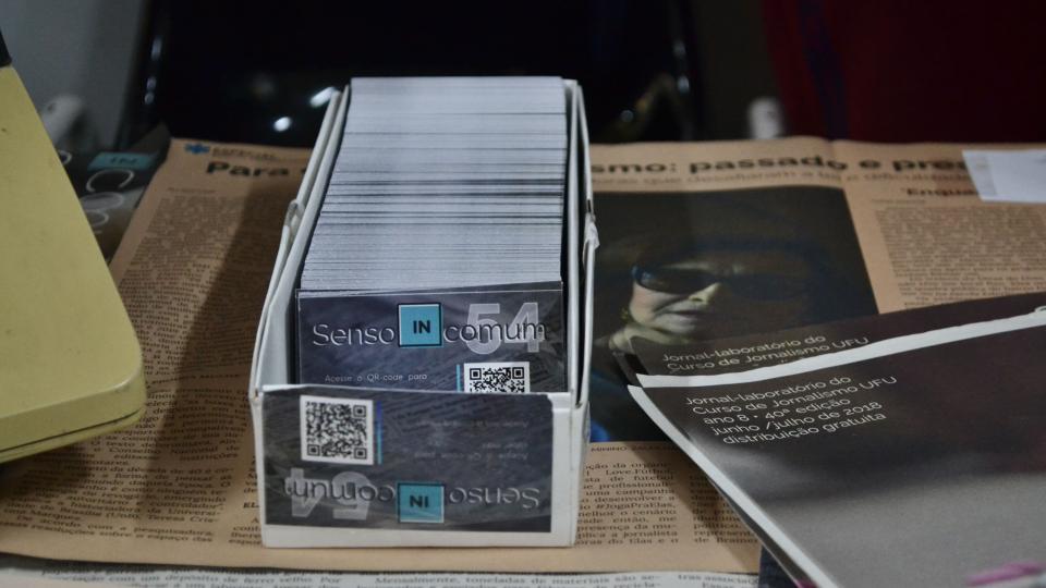 Cartões do jornal Senso (IN)comum em cima de edições impressas dele.