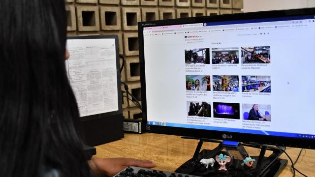 Pessoa com cabelo comprido preto, de perfil, visualizando a nova página do Comunica UFU na tela de um computador