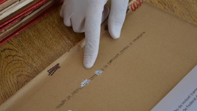 Imagem detalhe de um documento com a ponta do dedo indicador de um arquivista indicando o escrito