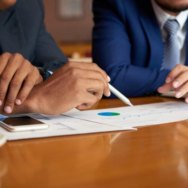 Foto colorida com empresários sentados à mesa analisando dados