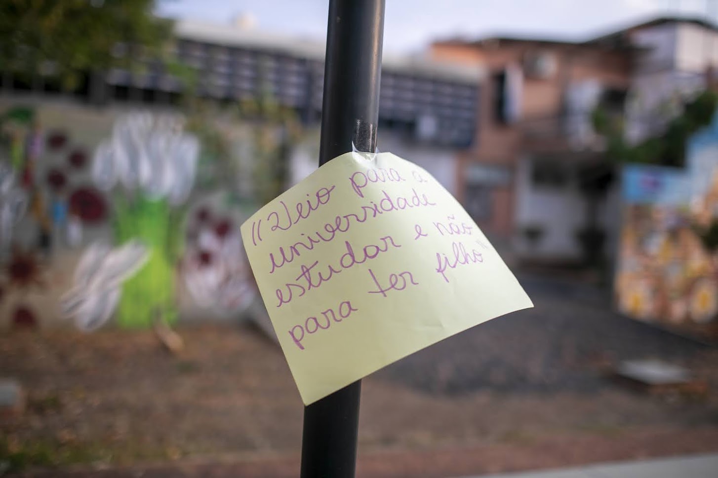 Imagem de cartaz afixado em um poste com os dizeres 'Veio para a universidade estudar e não para ter filho'; ao fundo, ambiente do Campus Santa Mônica, desfocado