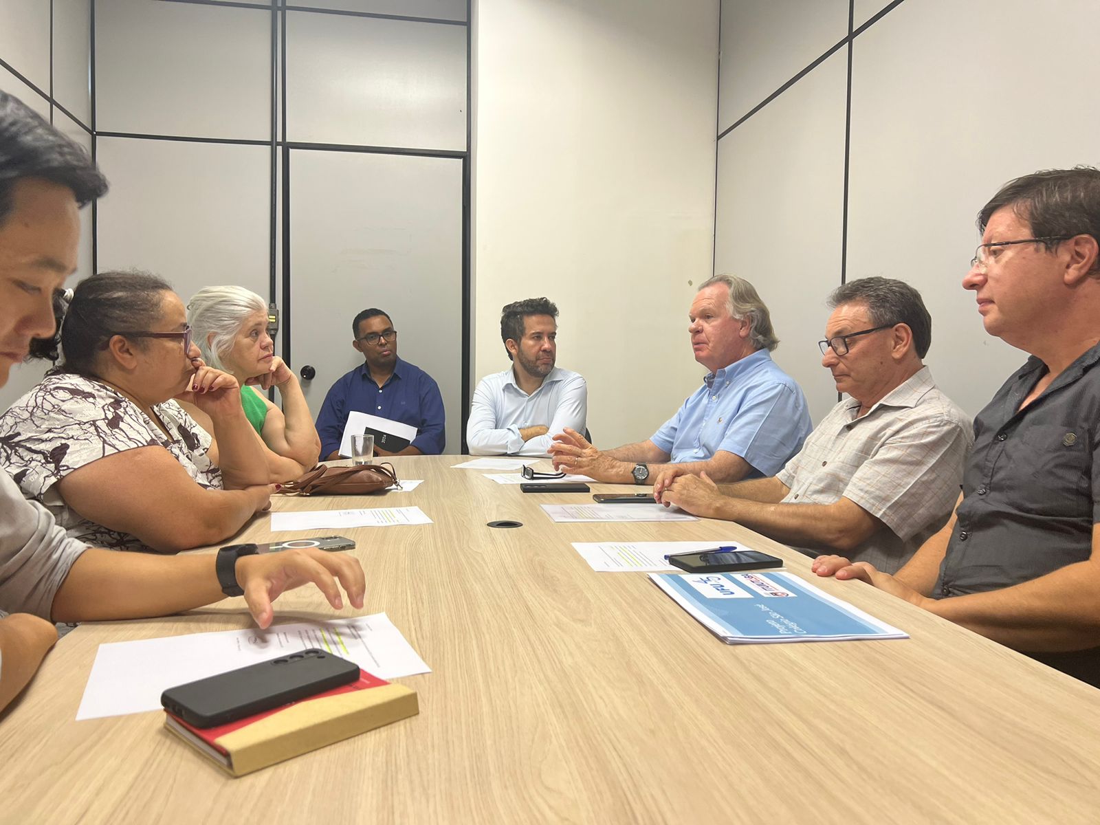 Imagem da reunião, com oito pessoas sentadas à mesa; deputado André Janones (com barba e camisa branca) aparece na cabeceira; à direita dele (com camisa azul clara e gesticulando), está o reitor Valder Steffen