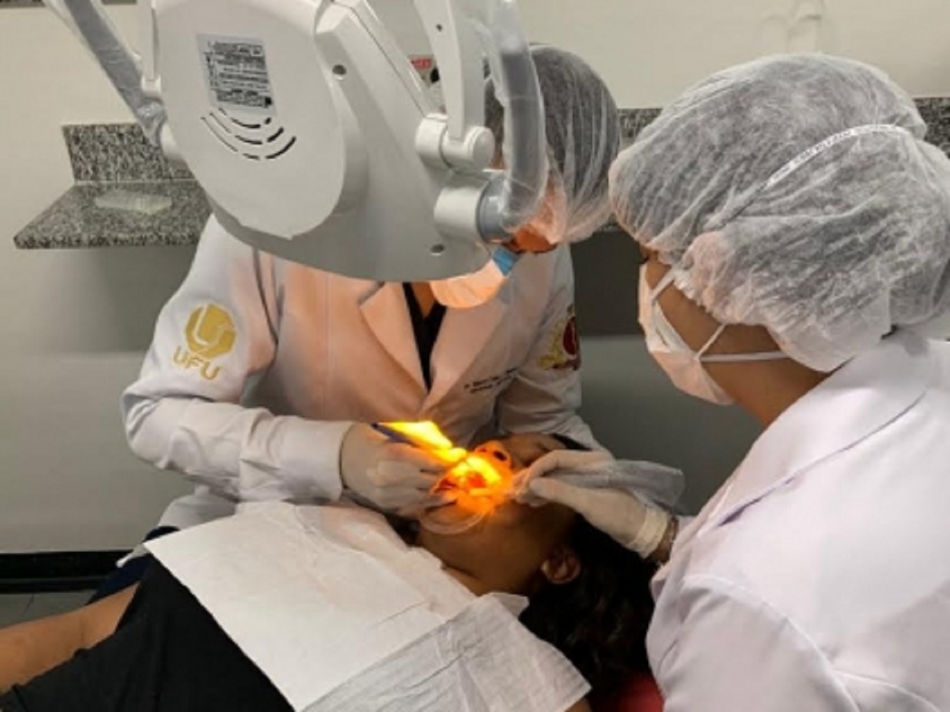 A imagem mostra duas profissionais de odontologia fazendo atendimento a paciente