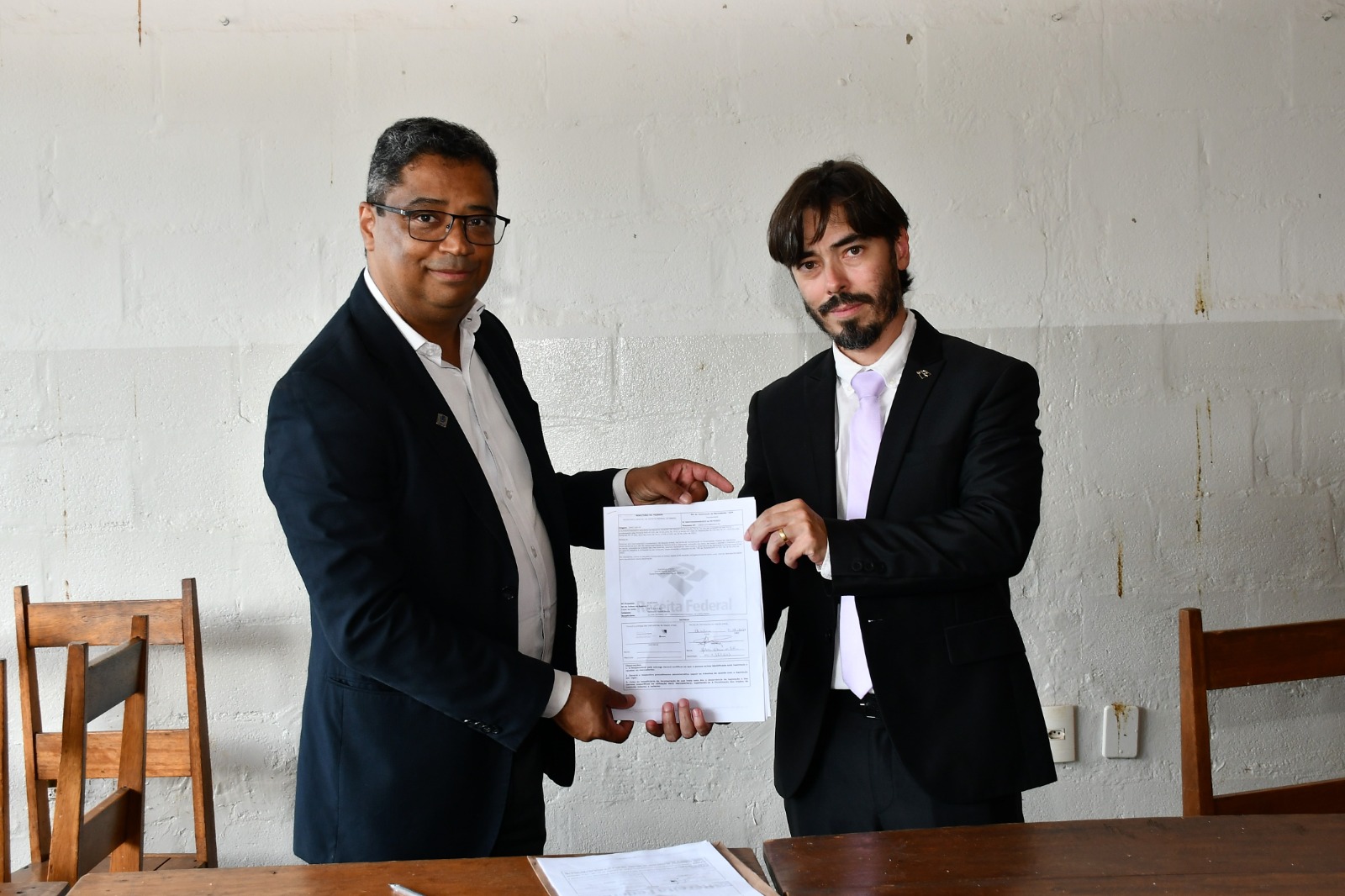 Imagem do pró-reitor Hélder Silveira (à esquerda) e do delegado Anderson Luiz da Silva exibindo o documento de doação dos materiais 