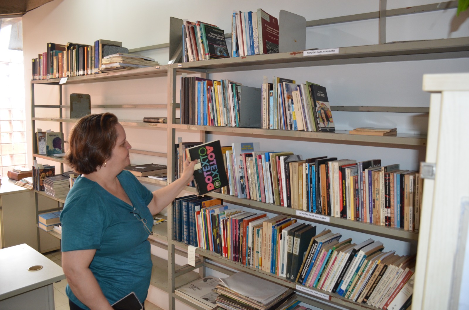 Mulher colocando livro numa estante de biblioteca