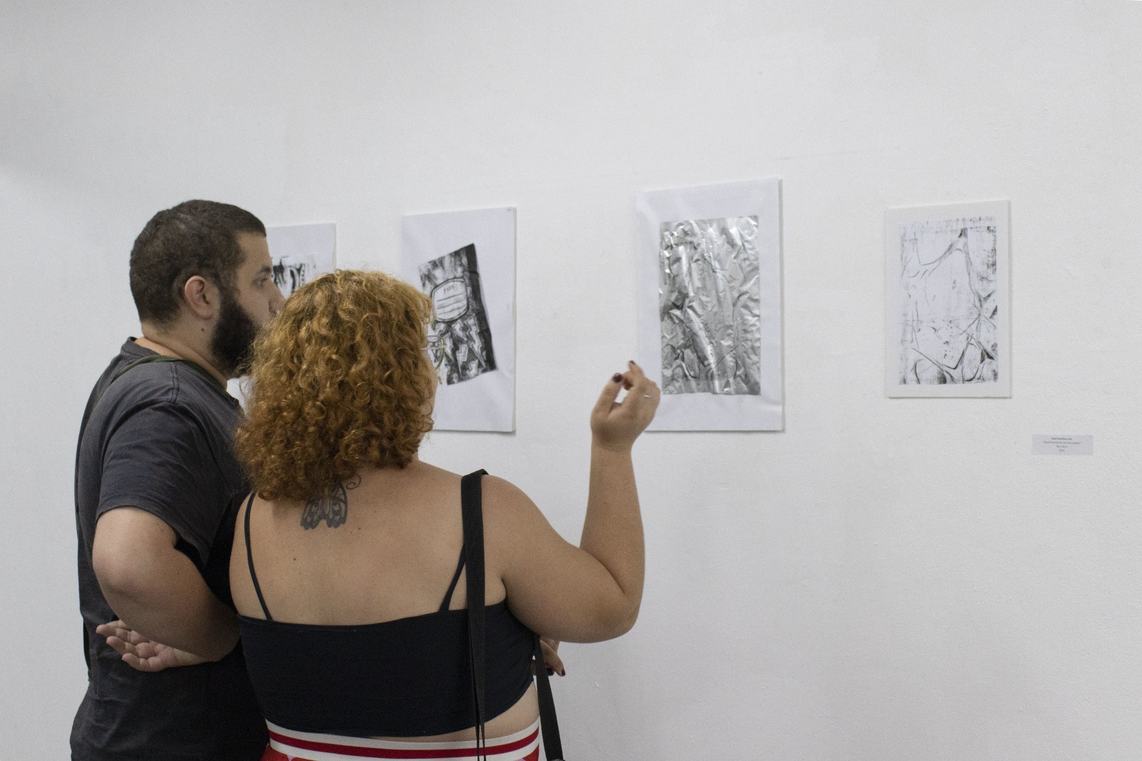 Na imagem, aparecem duas pessoas observando as obras da exposição