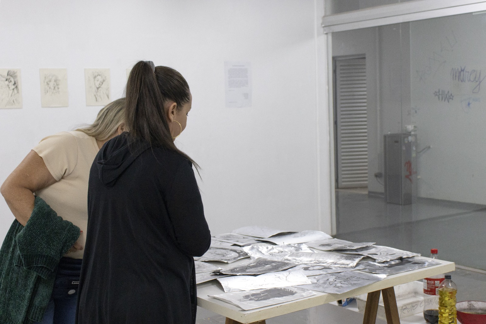 Na imagem, aparecem duas pessoas observando as obras da exposição