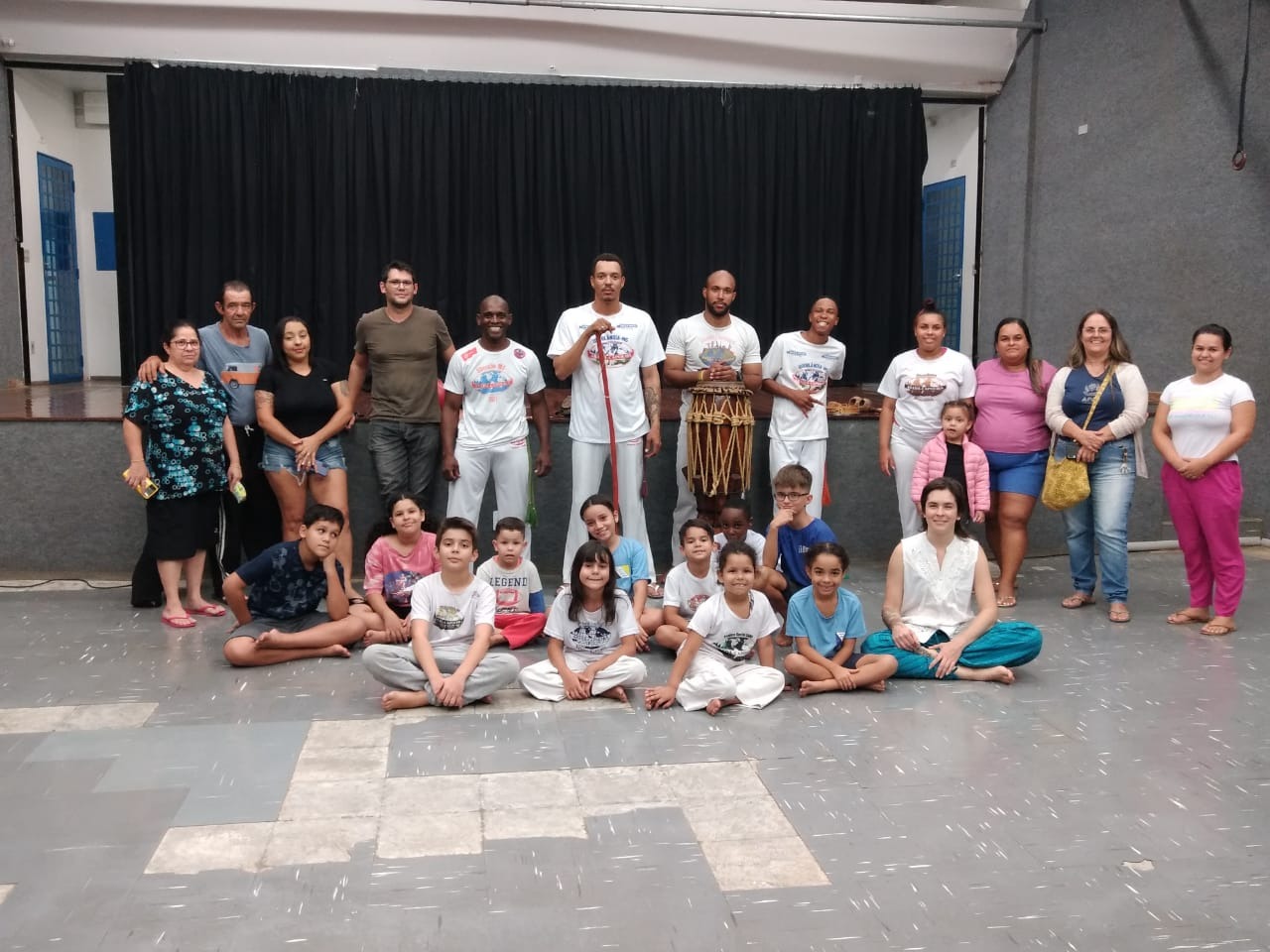 Pessoas em pé e algumas sentadas, segurando instrumentos musicais da capoeira