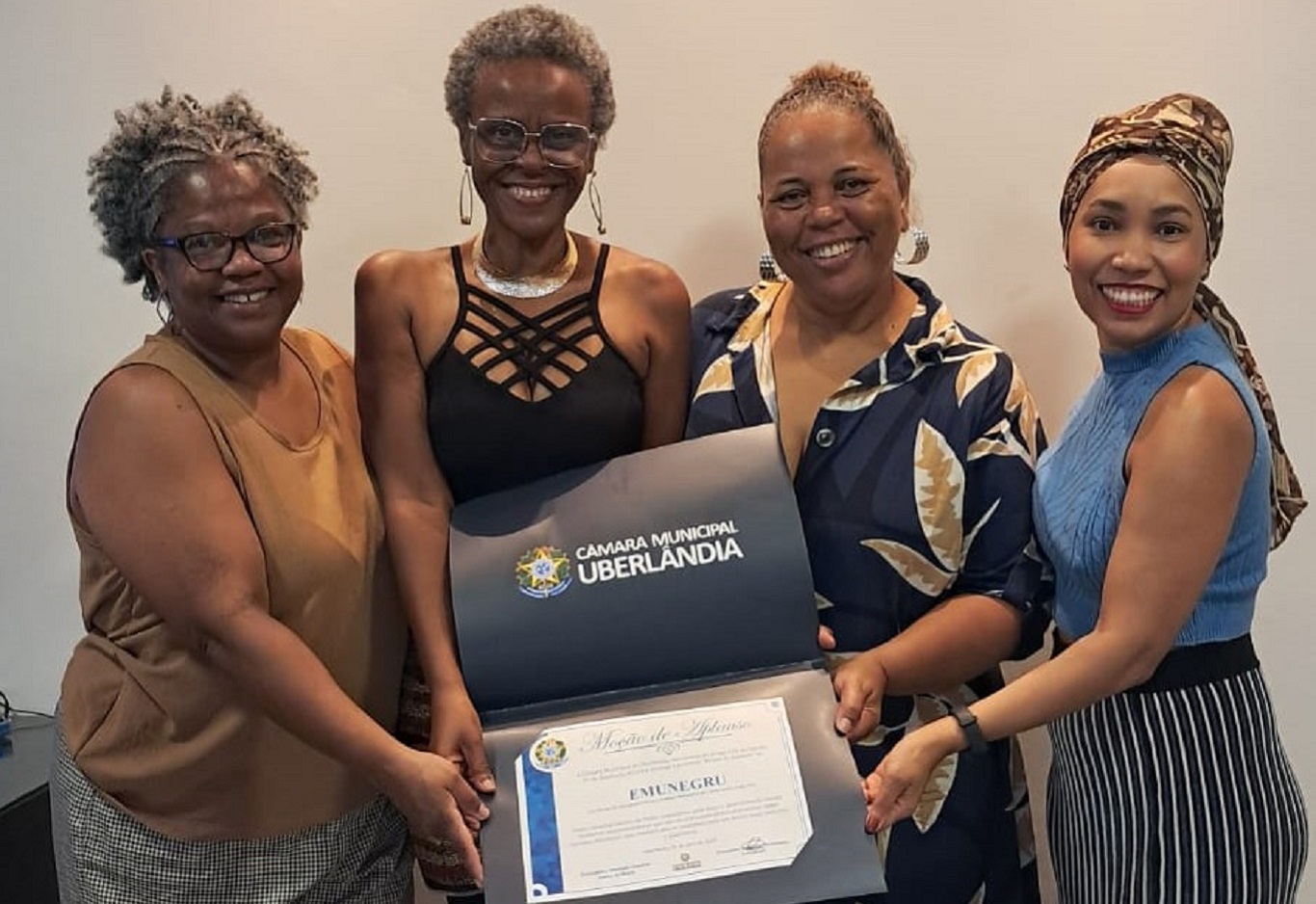 Na imagem, quatro mulheres negras segurando uma placa de homenagem.