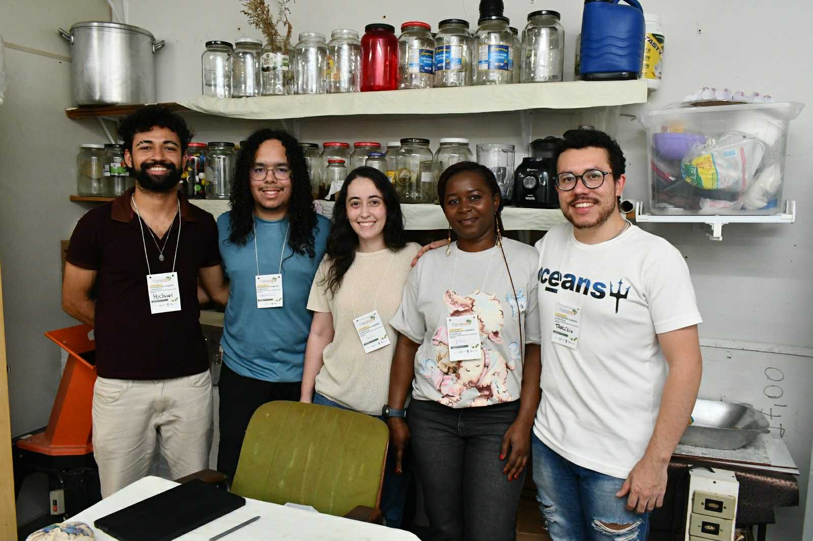 Grupo de cinco pessoas (três homens e duas mulheres); todos estão em pé e sorriem