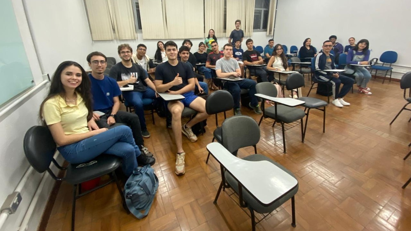 Imagem de uma sala de aula cheia de alunos sentados; ao fundo, dois professores estão em pé