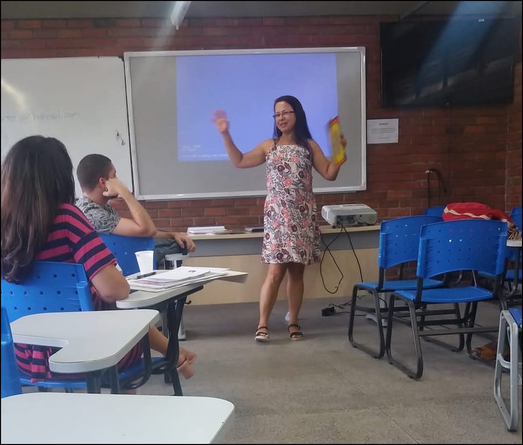 Maria Cristina apresentondo suas pesquisas em uma sala de aula com o retroprogetor atrás