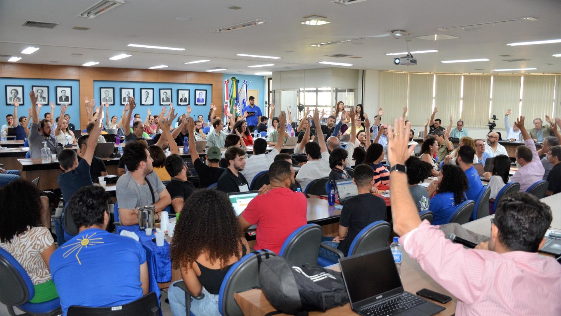 Momento de votação por parte dos conselheiros; alguns erguem os braços para manifestarem votos favoráveis, enquanto outros permanecem imóveis