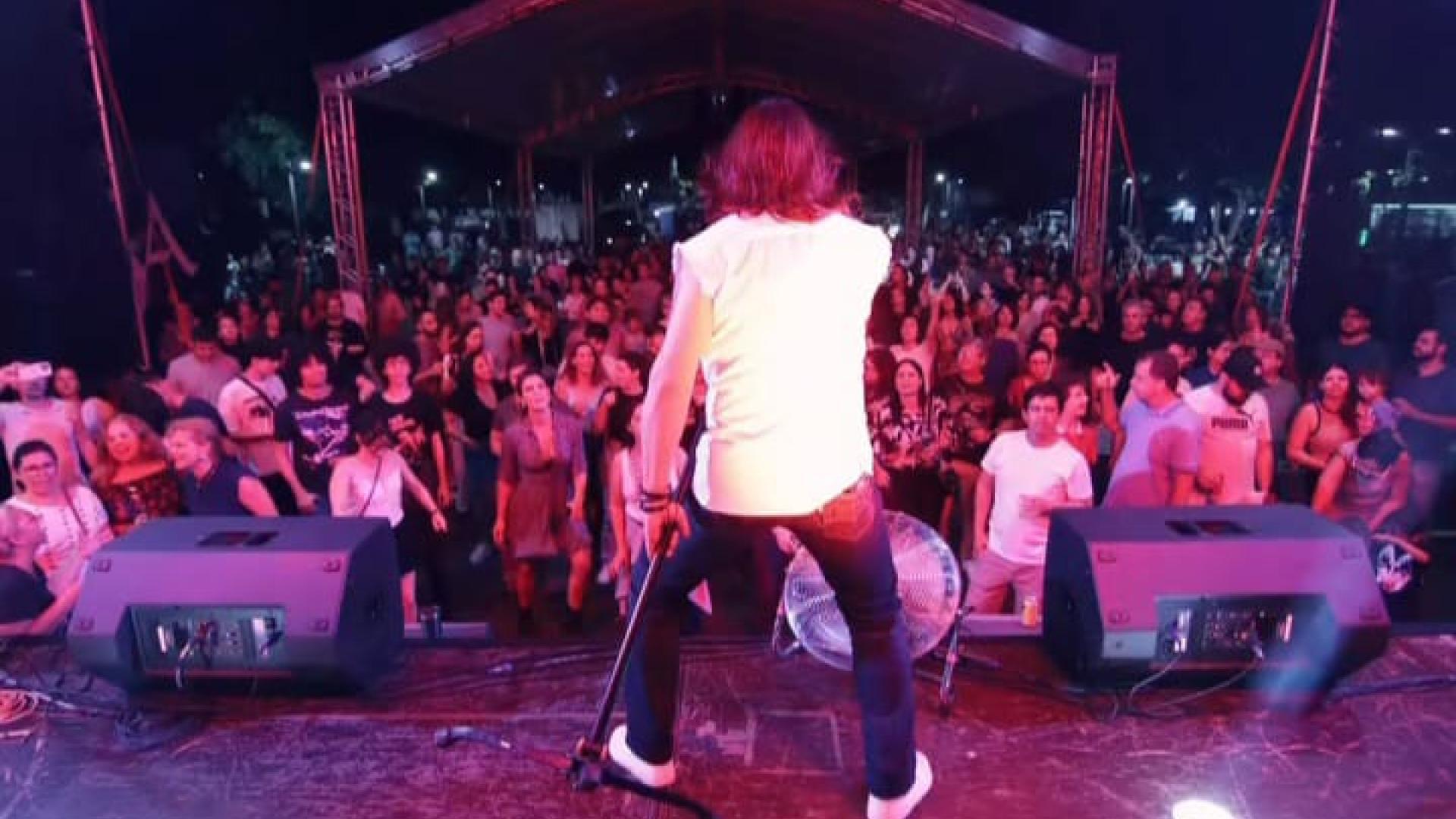 Homem de costas, em cima de um palco frente ao público, que o assiste cantar