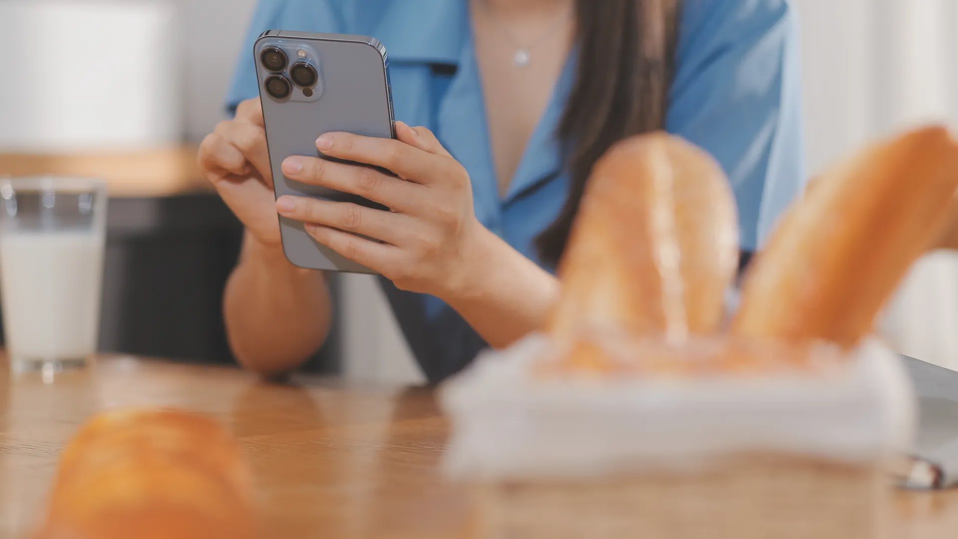 Foto de uma jovem utilizando o celular em uma mesa com pão e leite
