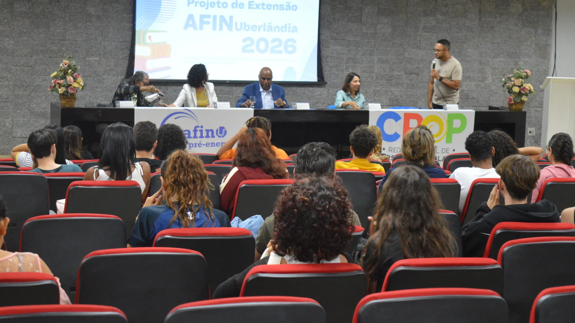 Imagem com os alunos do projeto Afin sentados observando a apresentação do professor Muriell Francisco da Costa, coordenador do projeto, que está ao lado de gestores da UFU