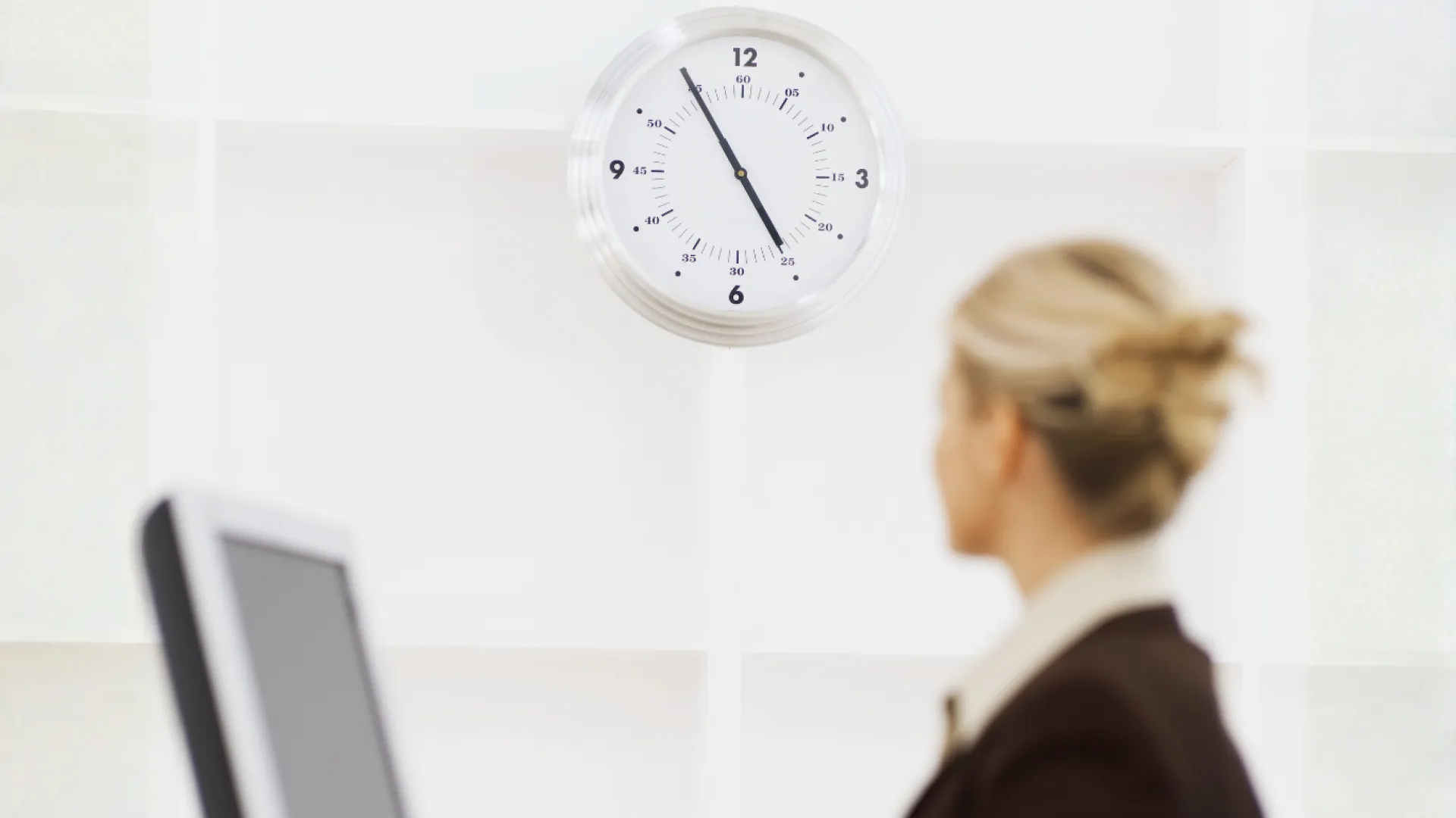 Trabalhadora em frente ao computador observa relógio ao fundo
