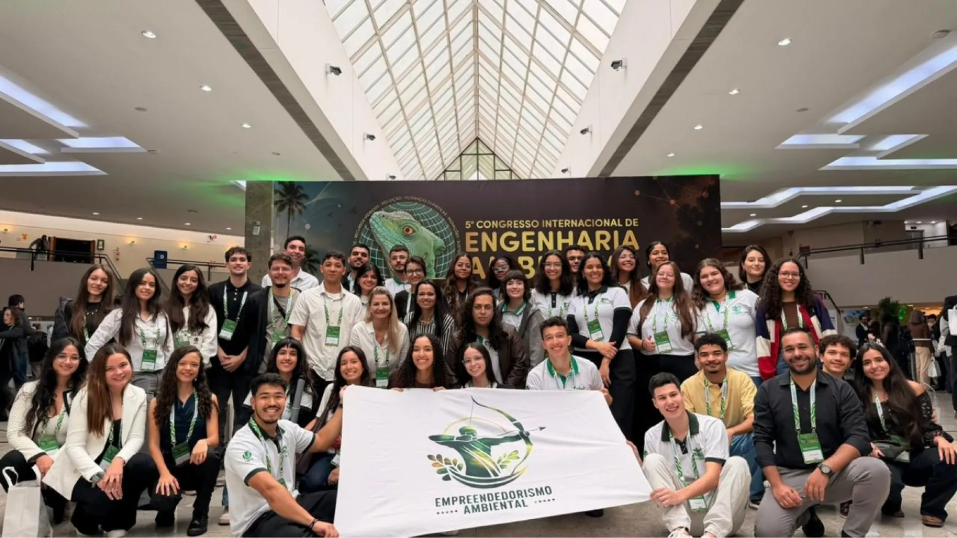 Participantes do Empreendedorismo Ambiental segurando bandeira do programa frente a um banner de congresso 