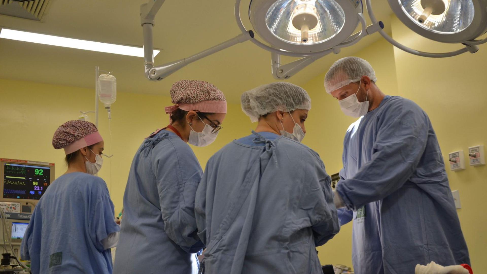 Médicos cirurgiões, sendo três mulheres e um homem, em uma sala de cirurgia, realizando o procedimento operatório