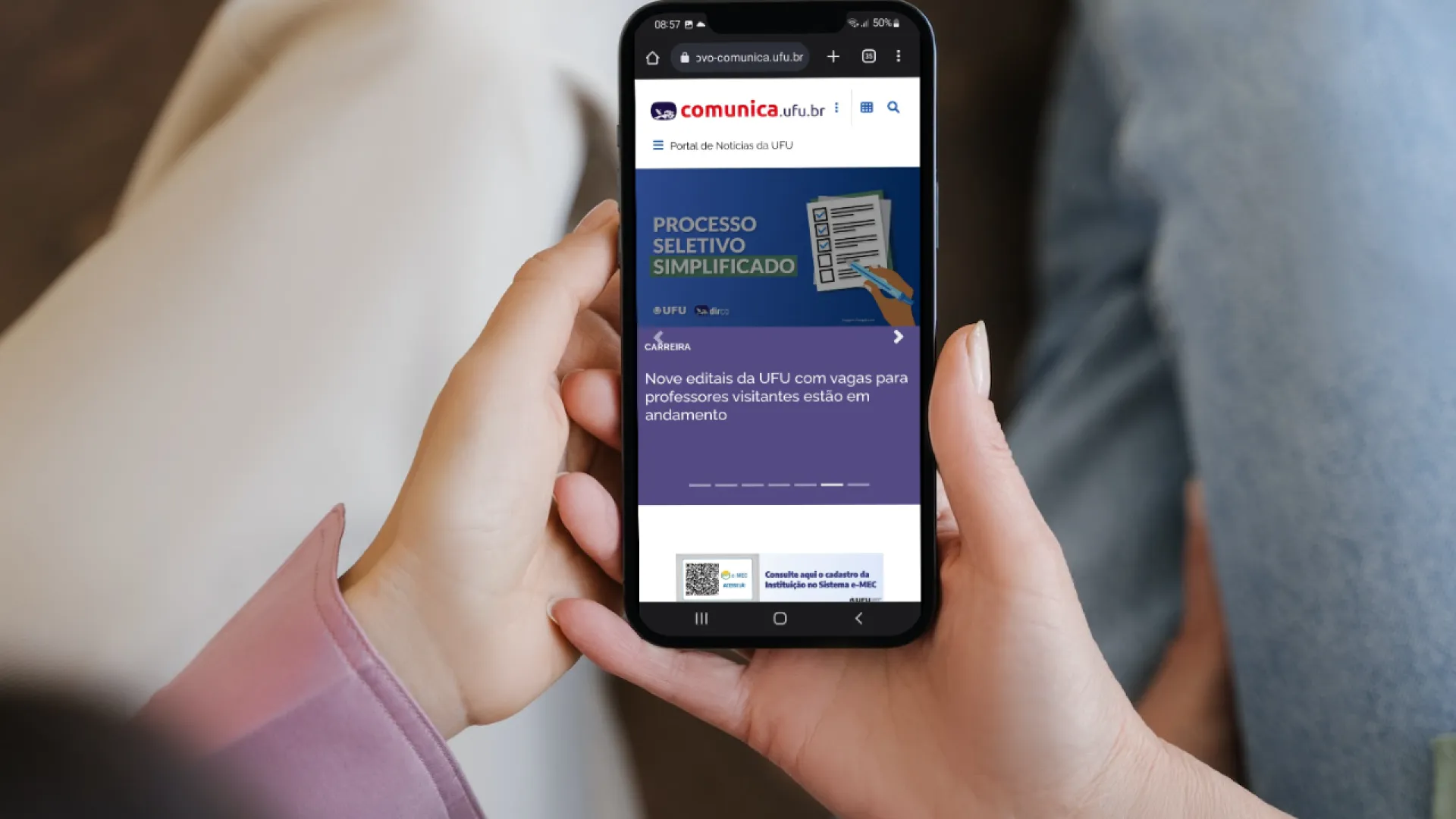 Mãos segurando um aparelho celular em que se vê o novo layout do Comunica UFU
