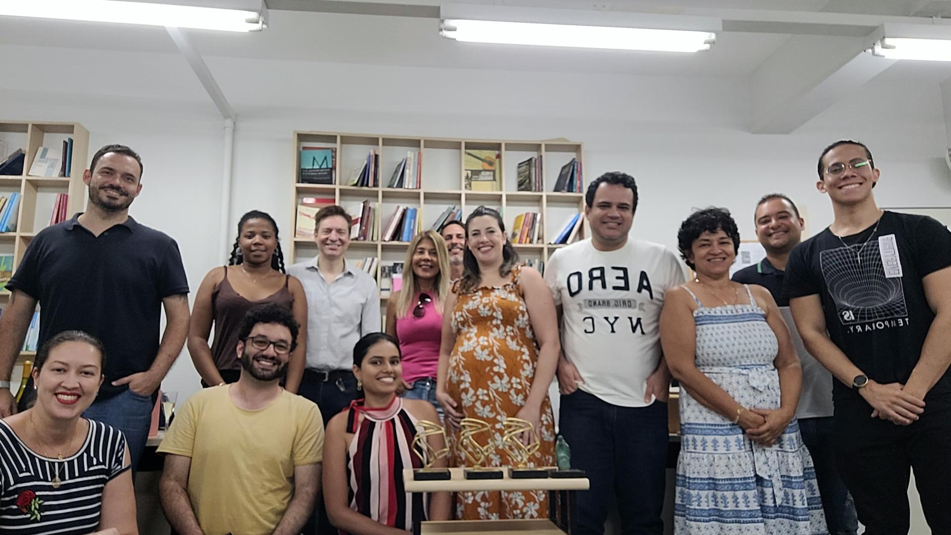 Imagem da atual equipe da Edufu, com 13 pessoas (sete homens e seis mulheres); três estão sentadas e 10 em pé; a maioria está sorrindo