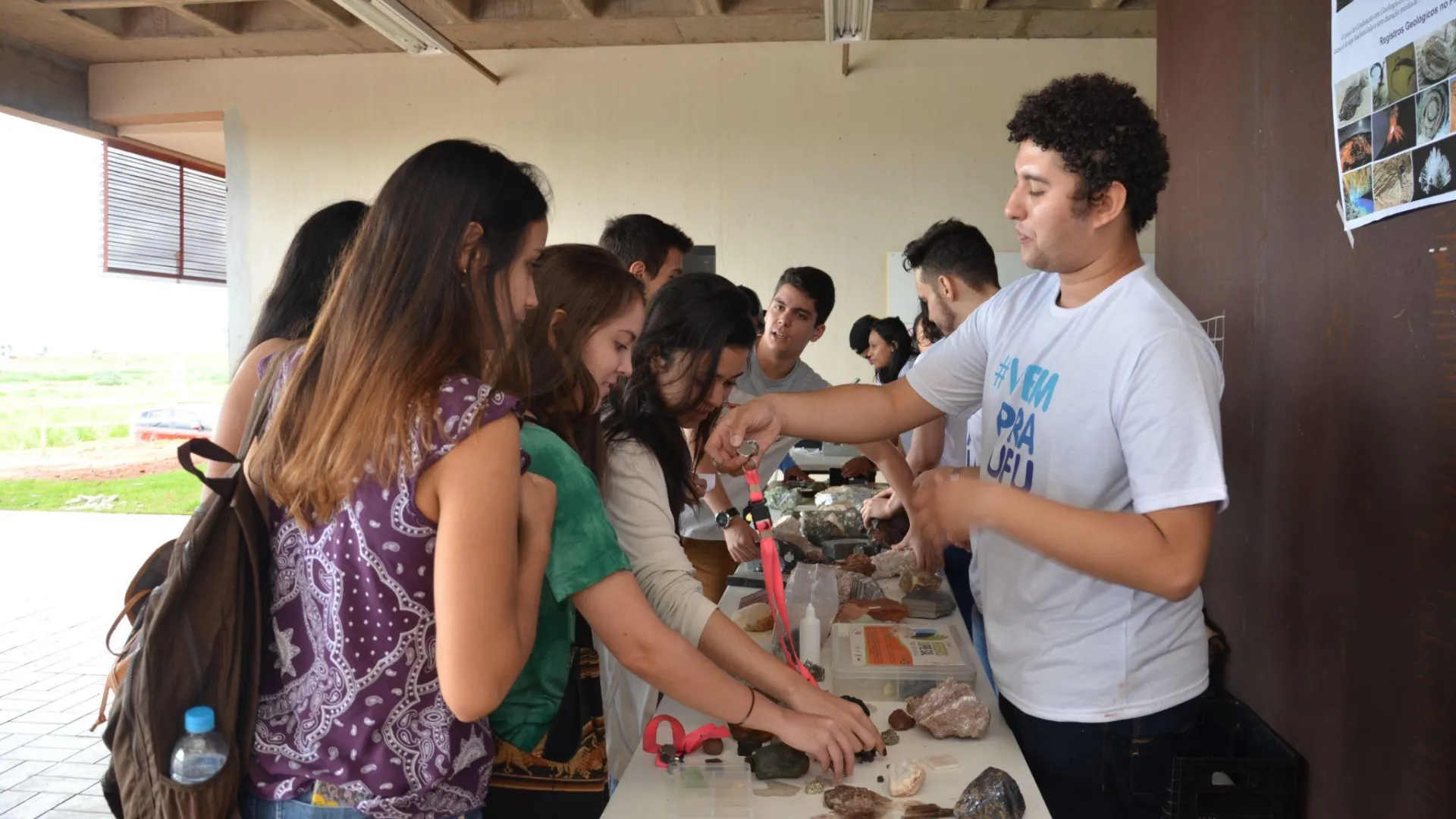 Acadêmico de graduação apresentando algumas rochas para grupo de estudantes do ensino médio