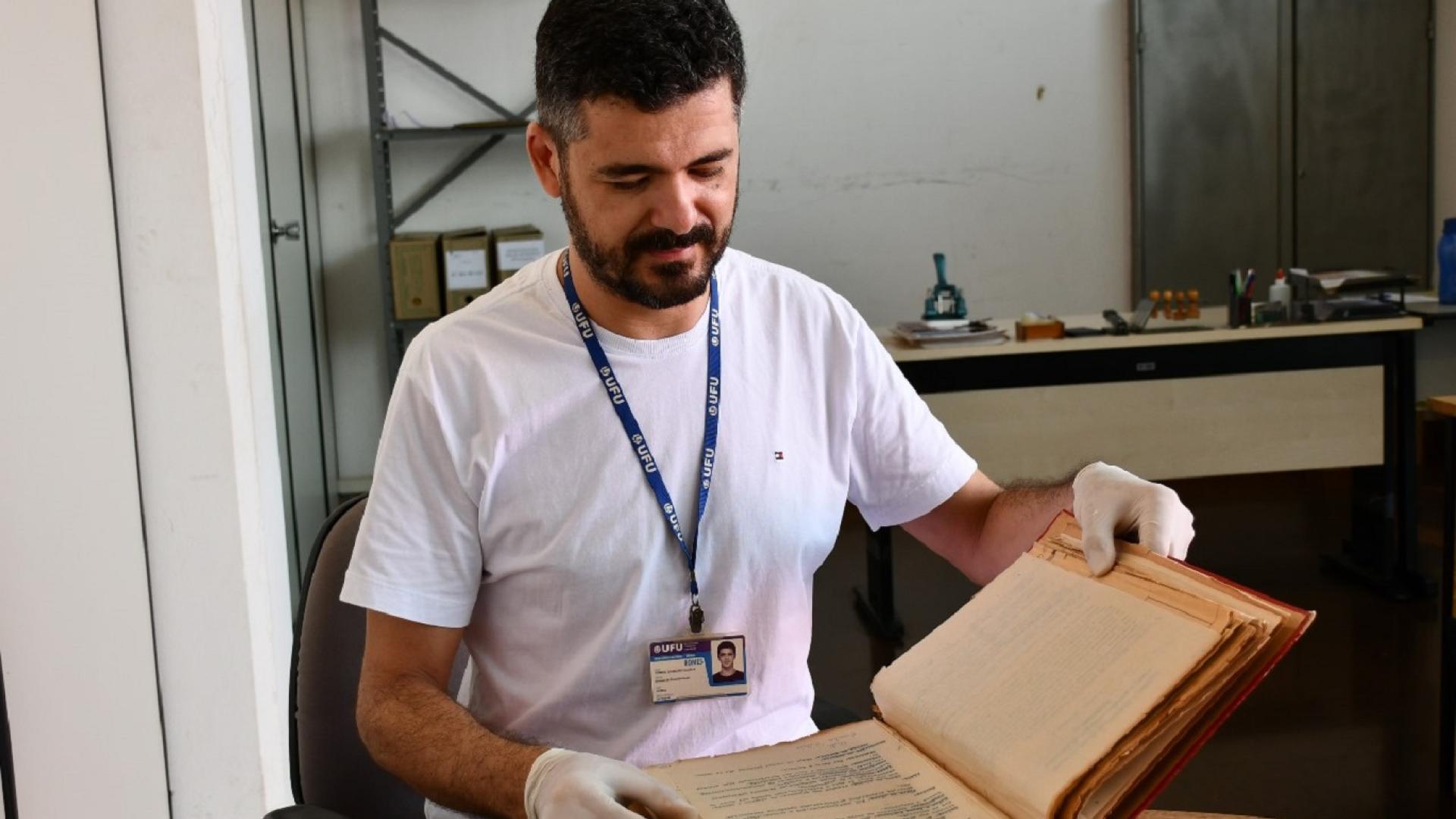 Arquivista segurando, sobre a mesa, um livro de registros antigos