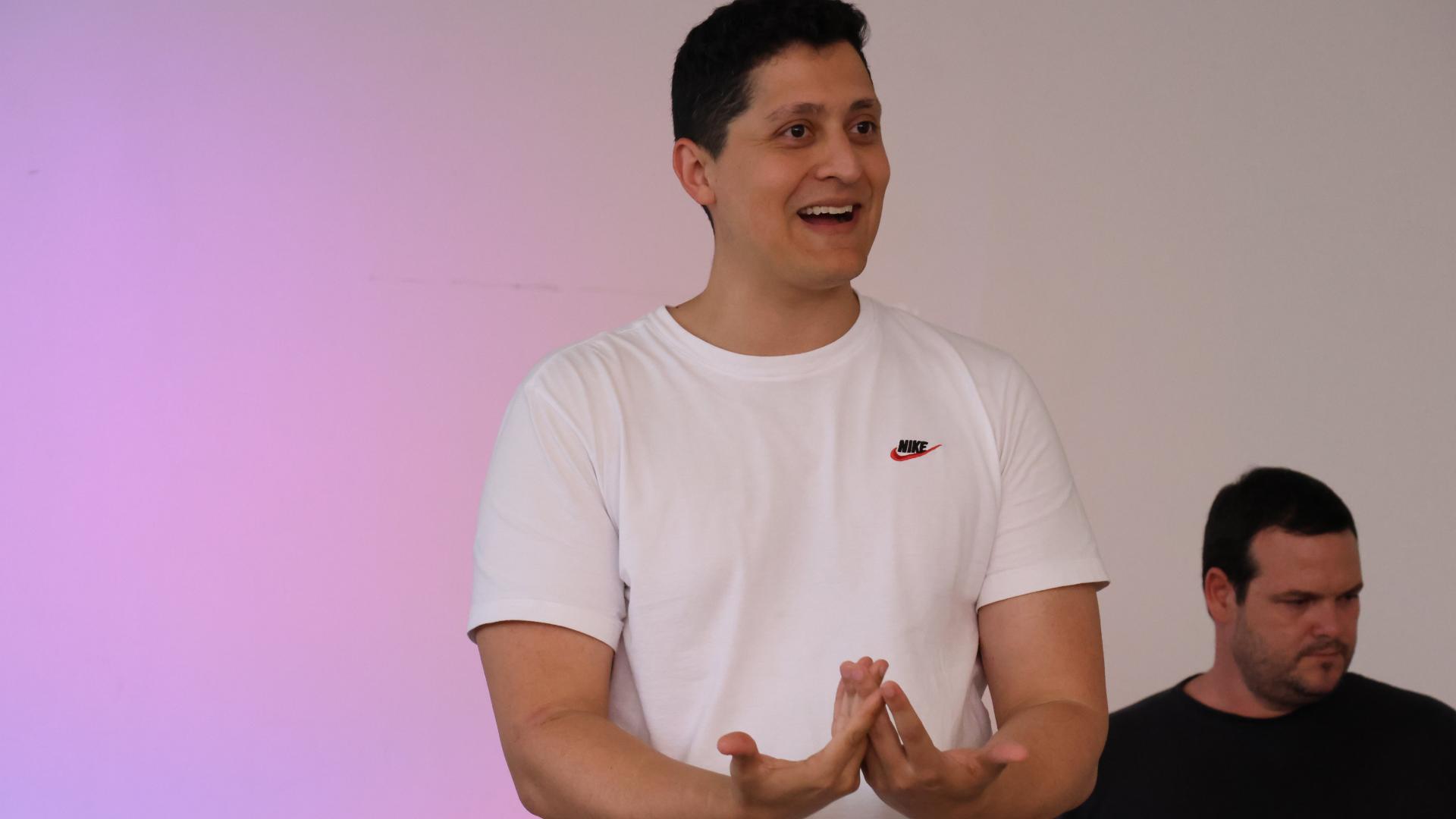 Imagem fechada de um homem vestido com camiseta branca, falando e gesticulando