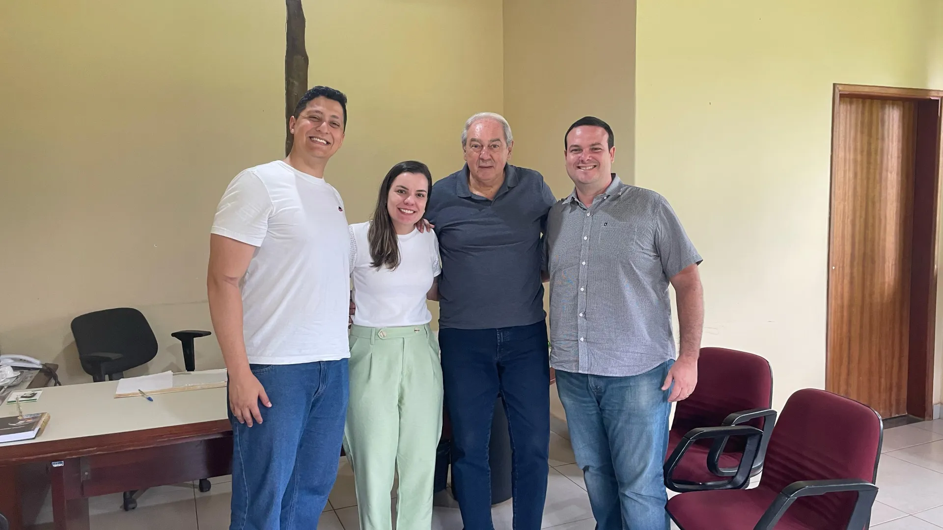 Quatro pessoas, uma ao lado da outra, abraçados. Sendo três homens e uma mulher, que está na segunda posição da esquerda para a direita