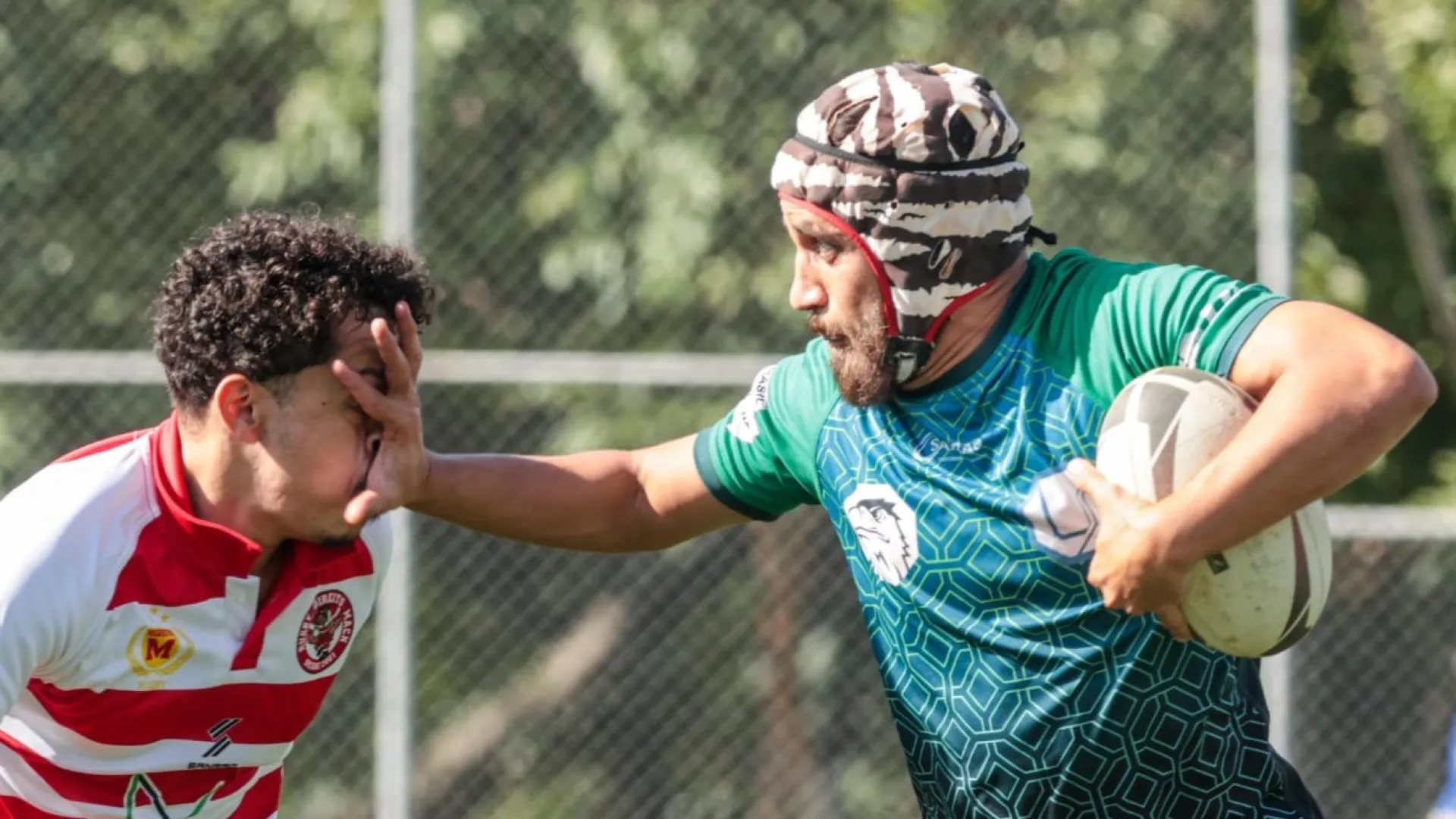Atleta da UFU segura bola de rugby e coloca a mão no rosto do adversário