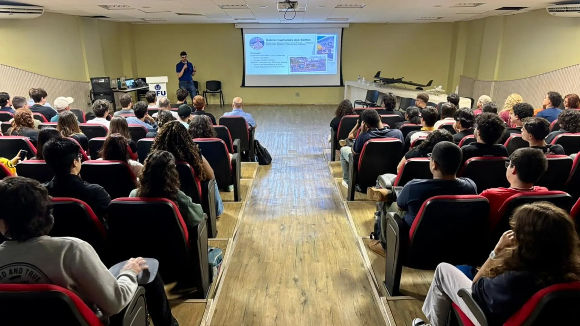 Imagem de fundo de um auditório cheio de estudantes assistindo uma palestra