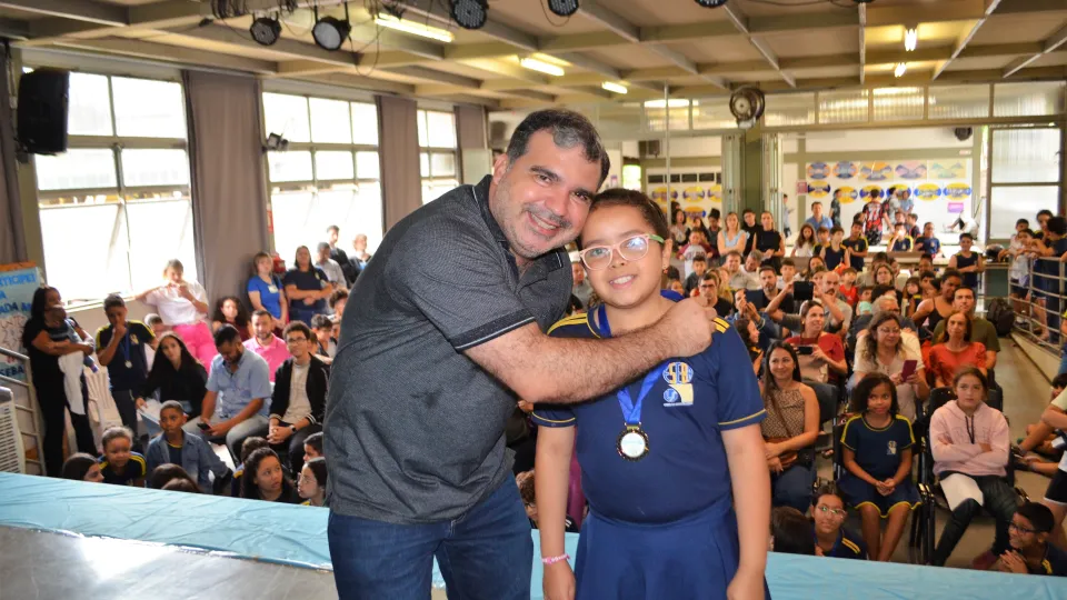 Um homem e uma menina posam para a foto. A menina tem uma medalha