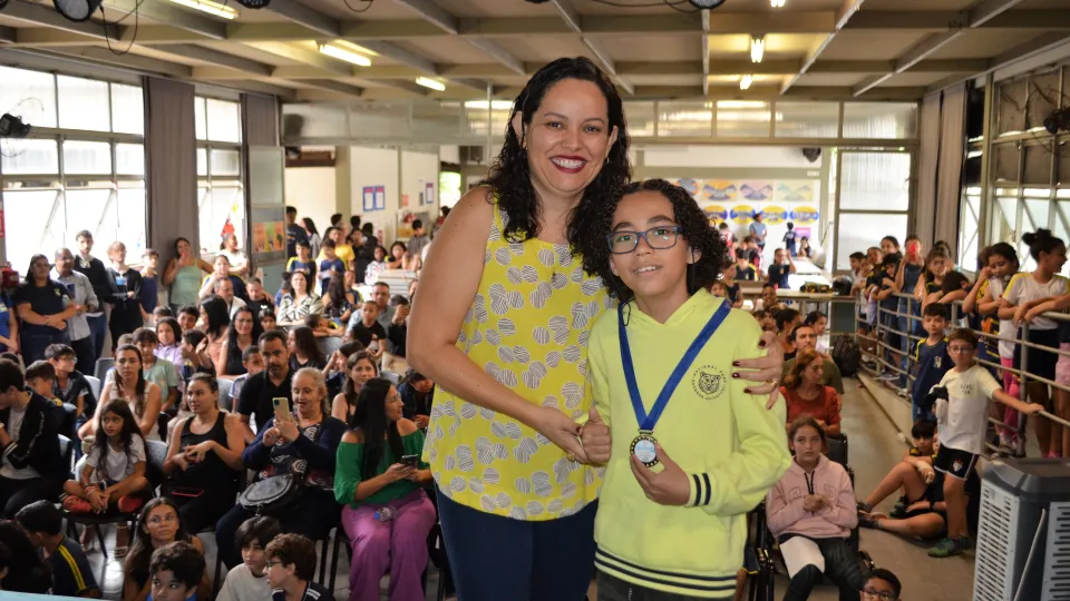 Uma mulher e um menino posam para a foto. O menino segura uma medalha