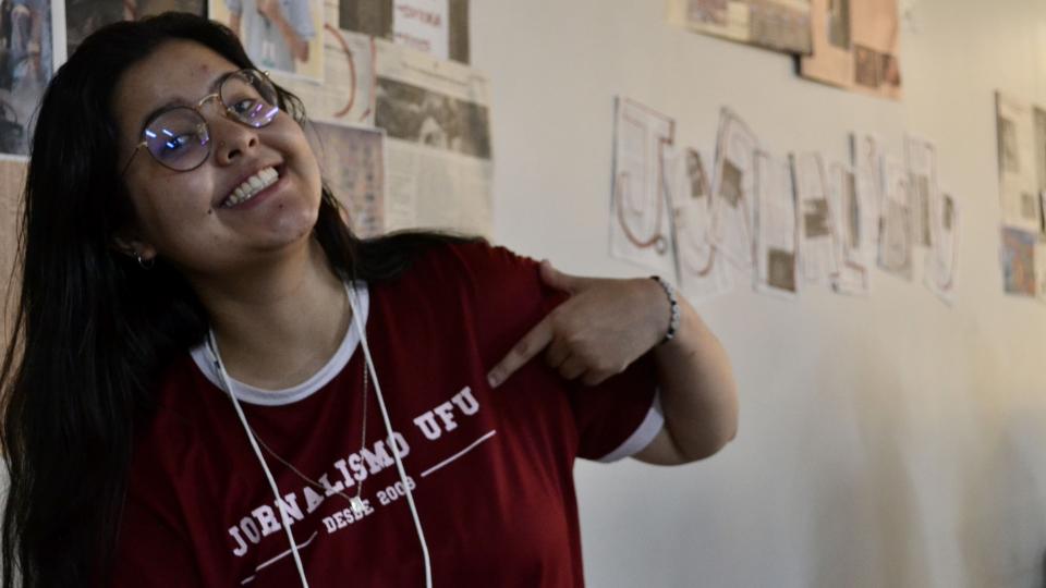 Estudante sorrindo e apontando para camiseta escrito "Jornalismo UFU"