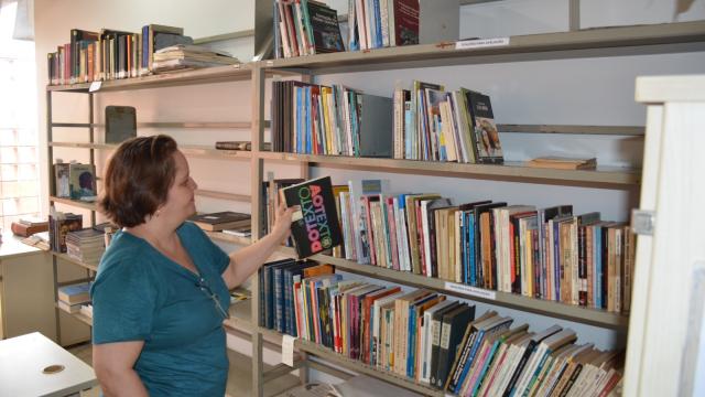 Mulher colocando livro numa estante de biblioteca