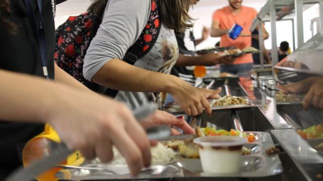 Imagem fechada em braços segurando bandejas para pessoas se servirem em um Restaurante Universitário