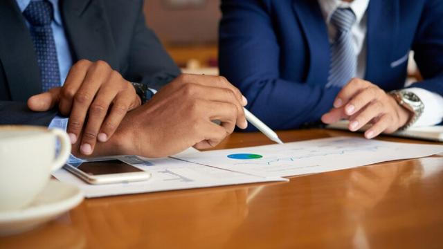 Foto colorida com empresários sentados à mesa analisando dados