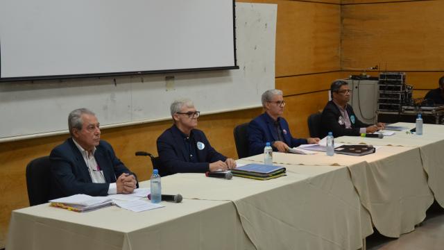 Imagem dos quatro candidatos a reitor da UFU, sentados, diante da mesa do auditório do Bloco 3Q, no Campus Santa Mônica