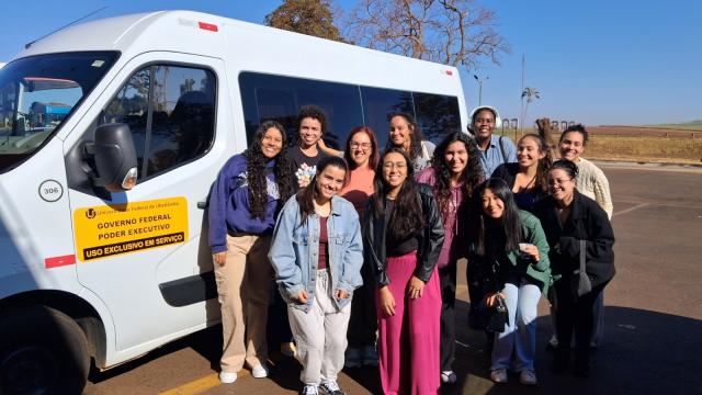 Foto de grupo com 12 pessoas em frente a uma van, na beira de uma rodovia