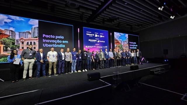 Imagem do palco do evento cheio, com 23 pessoas perfiladas