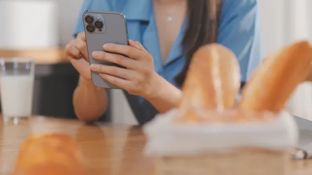 Foto de uma jovem utilizando o celular em uma mesa com pão e leite