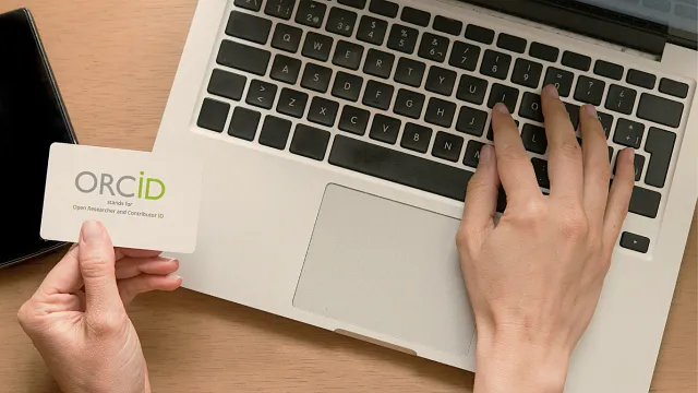 Pessoa com um cartão com o logo do ORCID na frente do computador