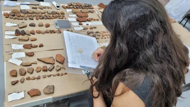 Imagem de moça fazendo anotações em uma tabela, diante de uma mesa com pedras