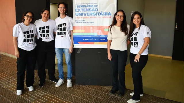 Cinco pessoas perfiladas ao lado do banner do evento (um homem e quatro mulheres)